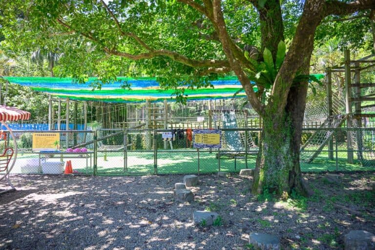 新竹統一渡假村馬武督渡假會議中心完整指南|山林住宿與親子週末攻略 11 新竹統一渡假村馬武督會議中心|樹、遊樂場、圍欄、繽紛遮陽布、石頭、泥土、草地。