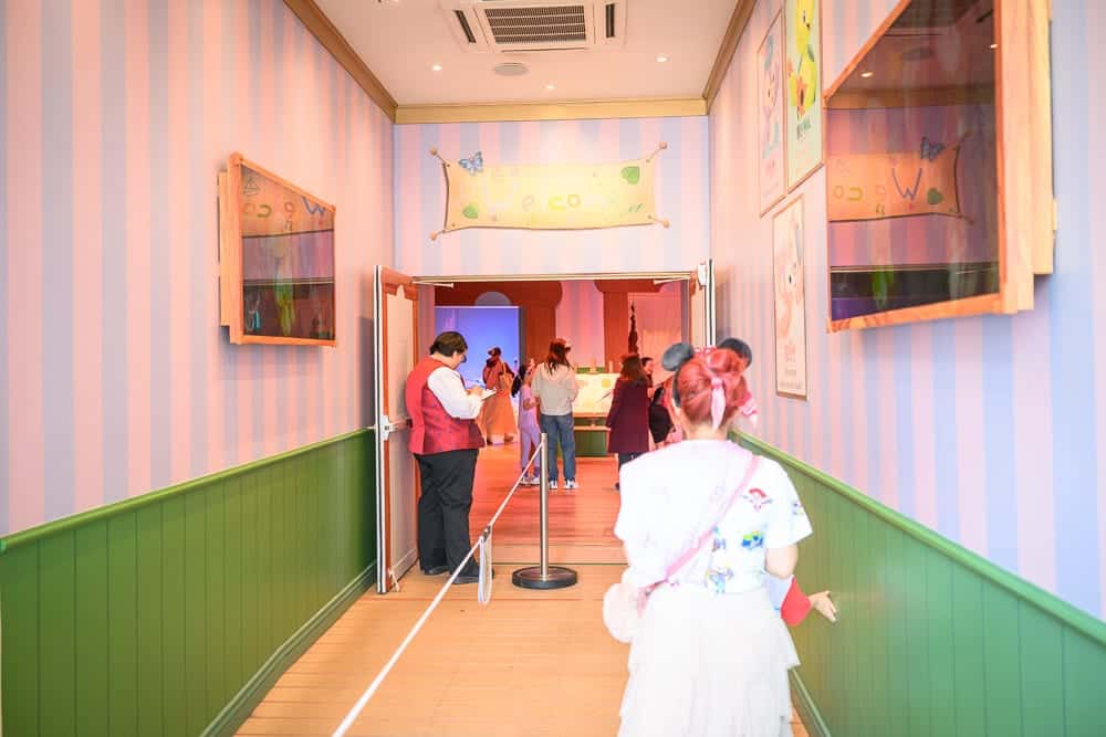香港迪士尼樂園｜走廊場景，粉藍色條紋牆壁，綠色踢腳板，木質地板，牆上掛有裝飾畫框，人們在走廊中行走，氣氛歡樂。