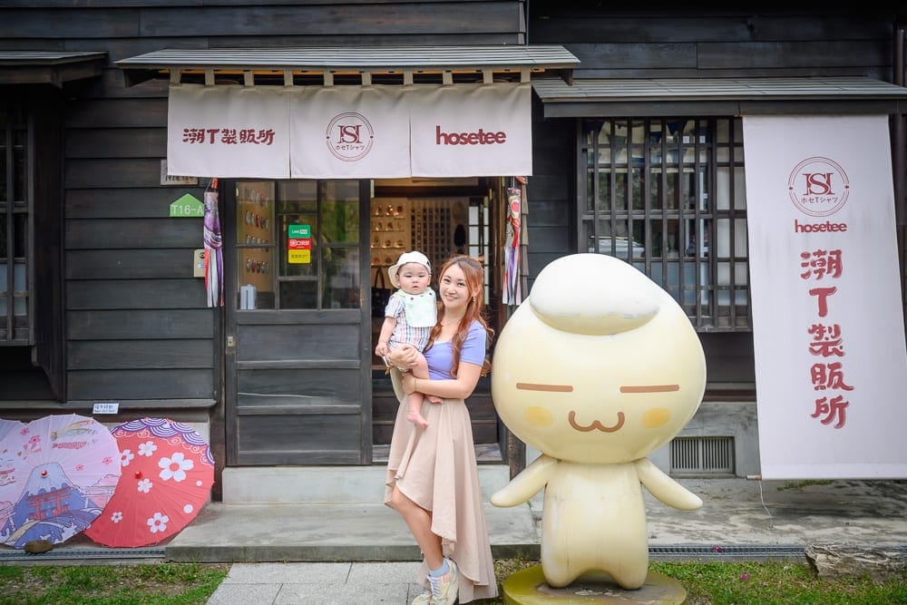嘉義檜意森活村龍貓｜商店外觀、門口，木造建築、遮陽棚、廣告布條，女人、嬰兒，卡通公仔，彩色雨傘。