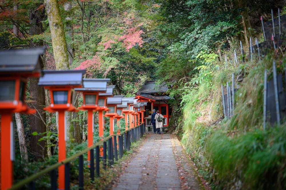 日本京都鞍馬寺修行之路｜石板路、紅色燈籠、樹林、草坡、鐵欄杆、建築，兩人。