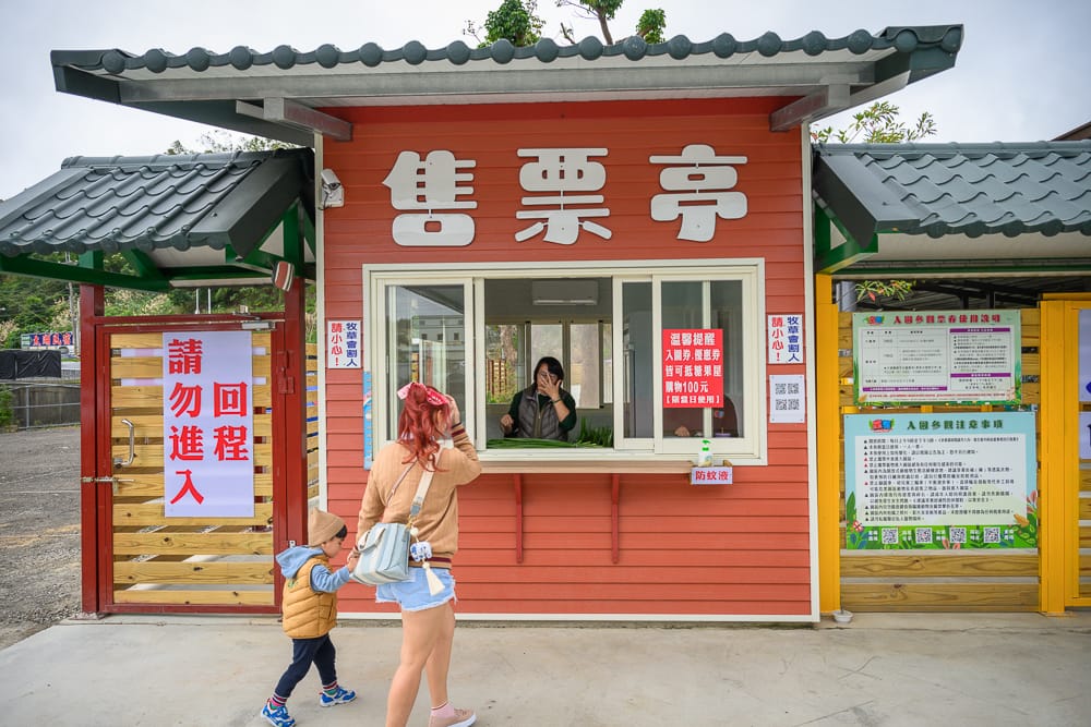 童萌農場紅色售票亭，媽媽牽小孩購票，窗台擺著餵食用牧草