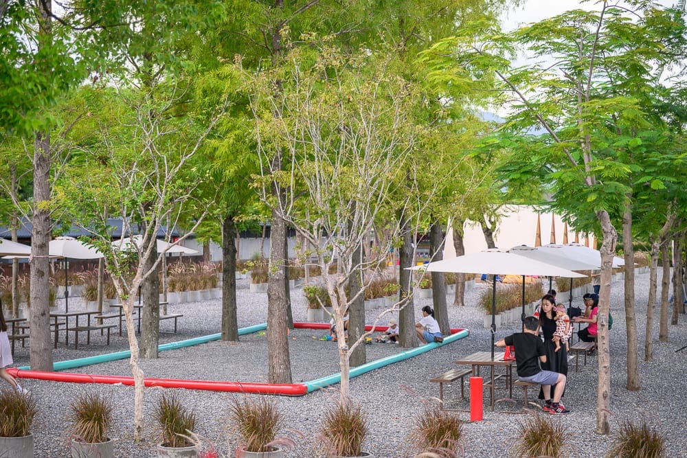 宜蘭樹懶餐廳｜樹林、碎石、桌椅、遮陽傘、草、盆栽、紅藍綠管、長椅、建築物。