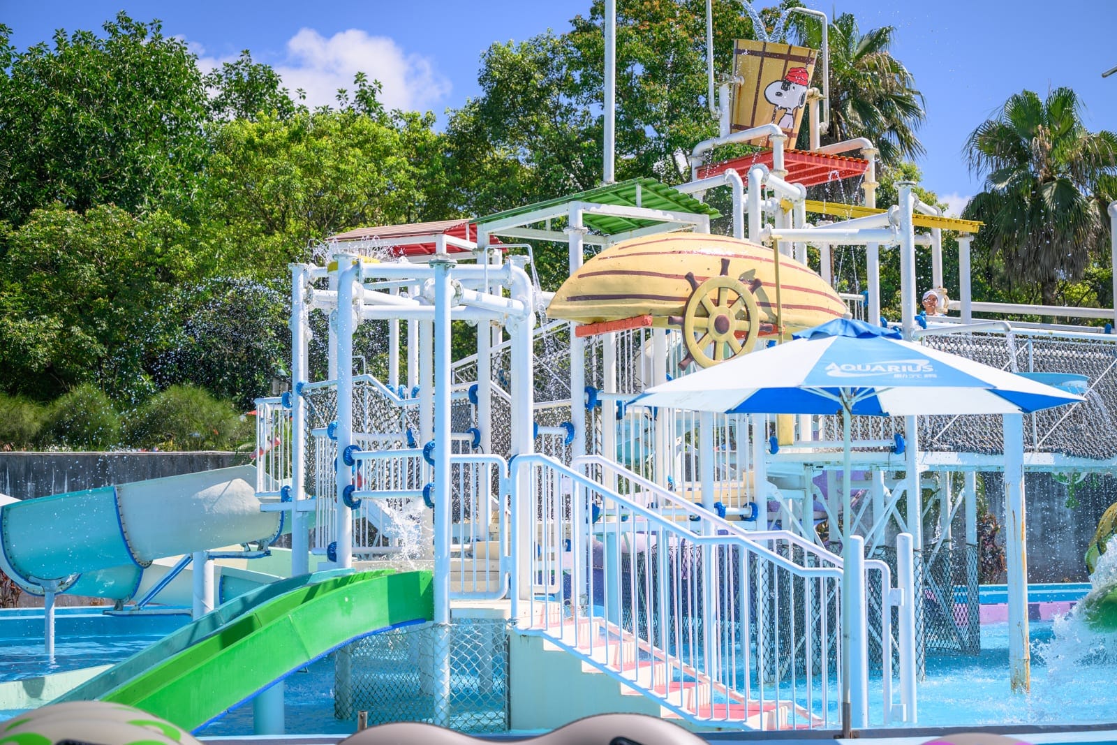 桃園六福水樂園｜水上樂園、遊樂設施、滑梯、遮陽傘、泳池、樹木、藍天。