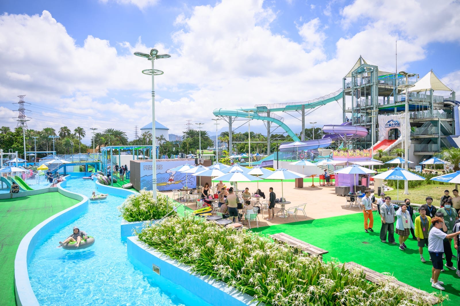新竹六福水樂園｜水上樂園、綠色草坪、遊樂設施、滑水道、泳池、遮陽傘、桌椅、遊客、樹木、藍天白雲。