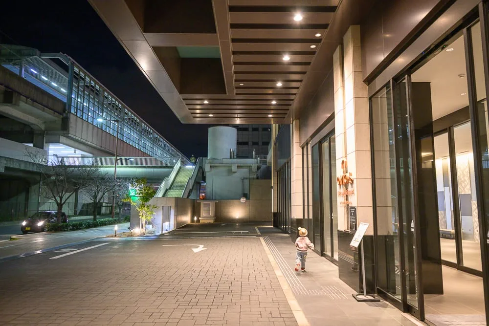 日本大阪 OMO 關西機場 by 星野集團完整攻略|大浴場・頂樓餐廳・機場交通 11 日本大阪-OMO關西機場|夜間街道、建築物、玻璃門、孩童、車道、天橋、燈光,石磚地面與現代化大樓外觀,透出寧靜與孤獨的都會夜景