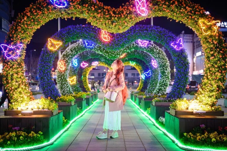 韓國釜山海雲台周邊美食｜女子、花拱門、蝴蝶燈飾、街道、夜晚，戶外場景充滿浪漫氛圍。