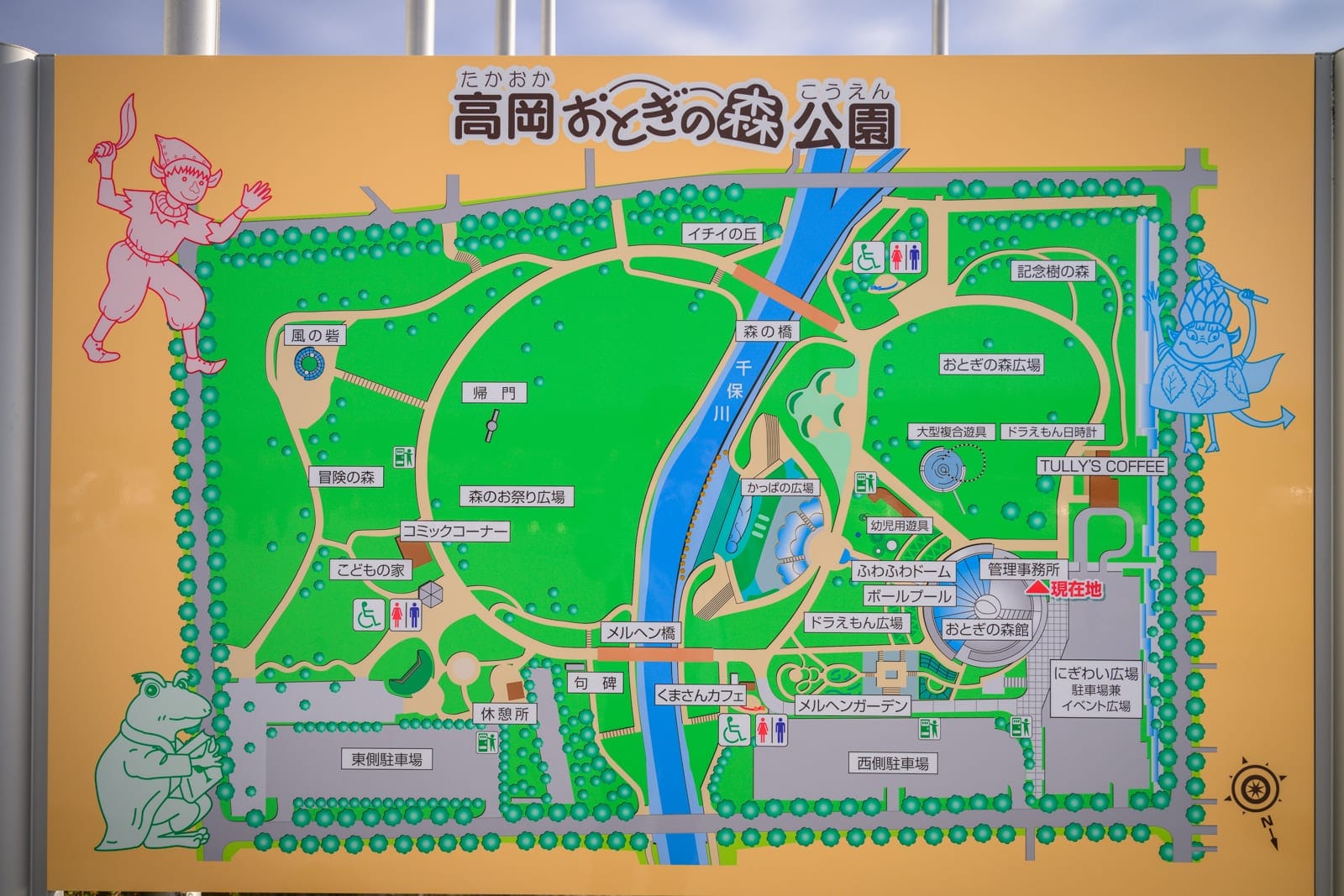 日本富山-高岡童話之森公園完整攻略|哆啦A夢雕塑與親子設施玩法解析 13 日本富山-高岡童話之森公園|黃色看板標示高岡童話森林公園地圖,圖面包含綠地、藍色河流、日文字標示、童話角色插圖,呈現戶外資訊導覽