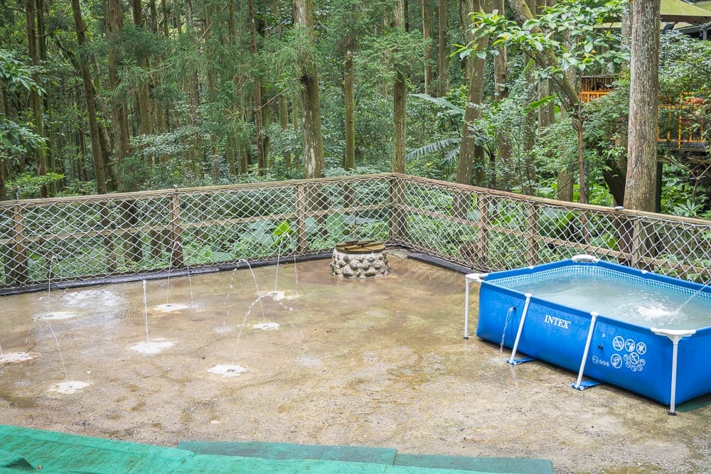 新竹馬武督探索森林完整攻略|森林步道與親子戶外設施 7 新竹馬武督探索森林|森林、圍欄、圓形石堆、藍色泳池、白色水管、綠色植被、樹木、雨水噴泉。