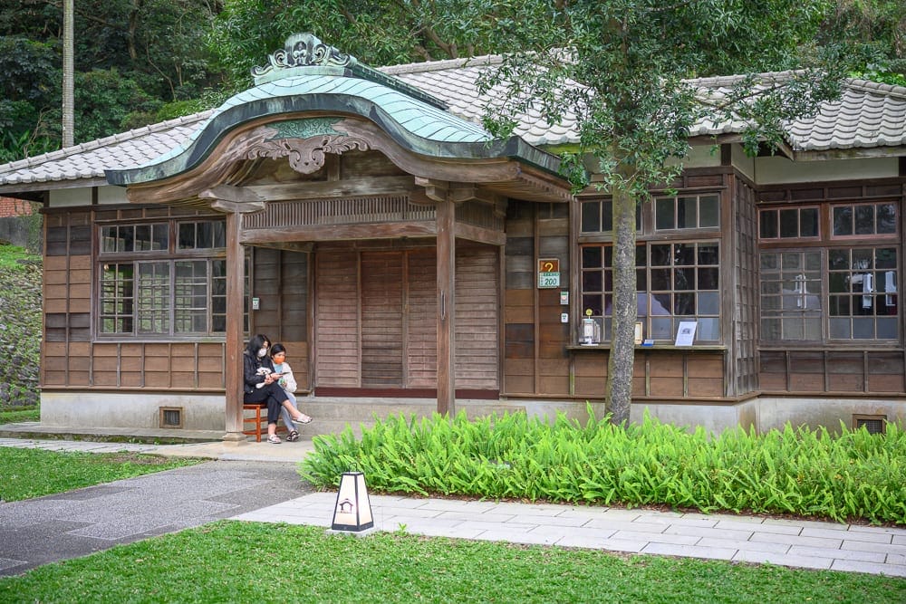 桃園神社｜日式木造建築，古蹟，庭園，草地，石板路，兩名女子坐於走廊休息，綠樹，屋頂，木牆，窗戶，寧靜氛圍。