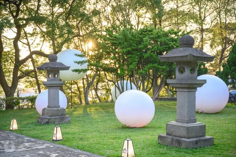 桃園神社｜草地、石燈籠、圓形發光球體、樹林、夕陽，黃昏時刻的戶外庭園散發出柔和光芒，營造出寧靜且神祕的氛圍。