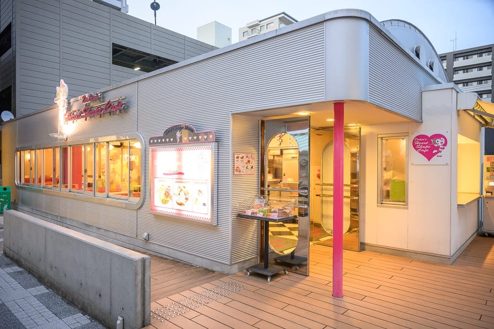 日本仙台-麵包超人博物館｜街道、金屬建築、咖啡廳、玻璃窗、招牌、木地板，傍晚時分的光線柔和，外觀呈復古風格，門口帶有粉紅色柱子