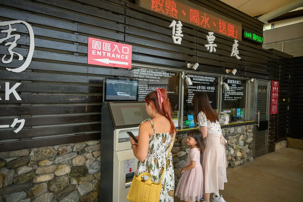 新北野柳地質公園完整攻略|女王頭奇岩怪石玩法解析 9 新北野柳地質公園|售票處、售票機、遊客、木造牆面、指示牌,幾位女性與孩童站在木質外牆的售票處前,其中一人操作著自動售票