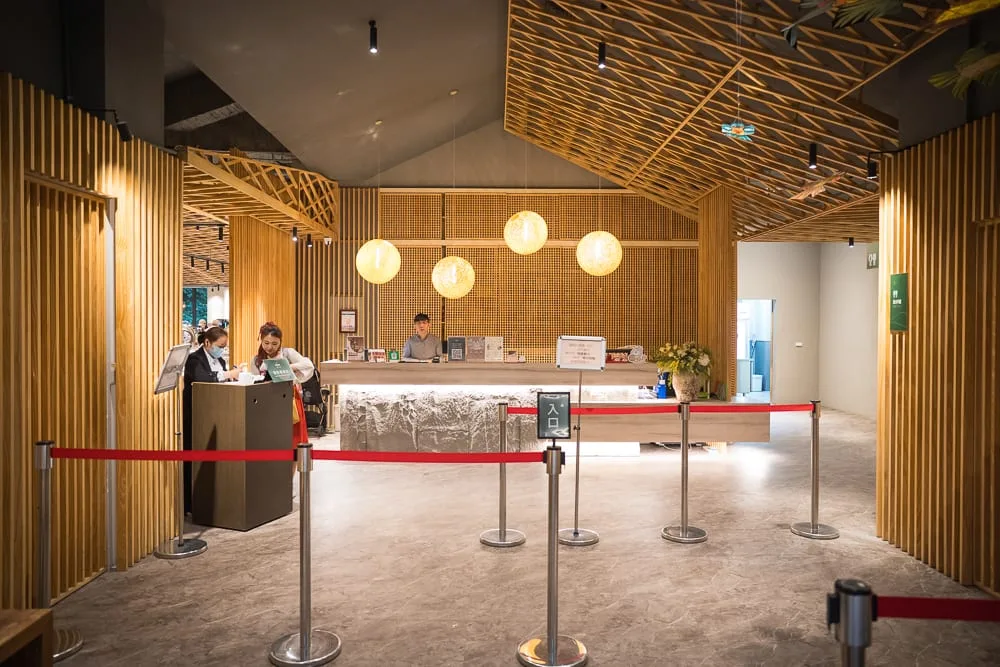 南投溪頭福華渡假飯店完整攻略|漢光樓住宿體驗與夜間生態導覽 9 南投溪頭福華飯店|室內、櫃檯、圓燈、木條、紅龍柱、人員,木質裝潢空間設有服務櫃檯與圓形吊燈,前方拉起紅色排隊動線阻隔。