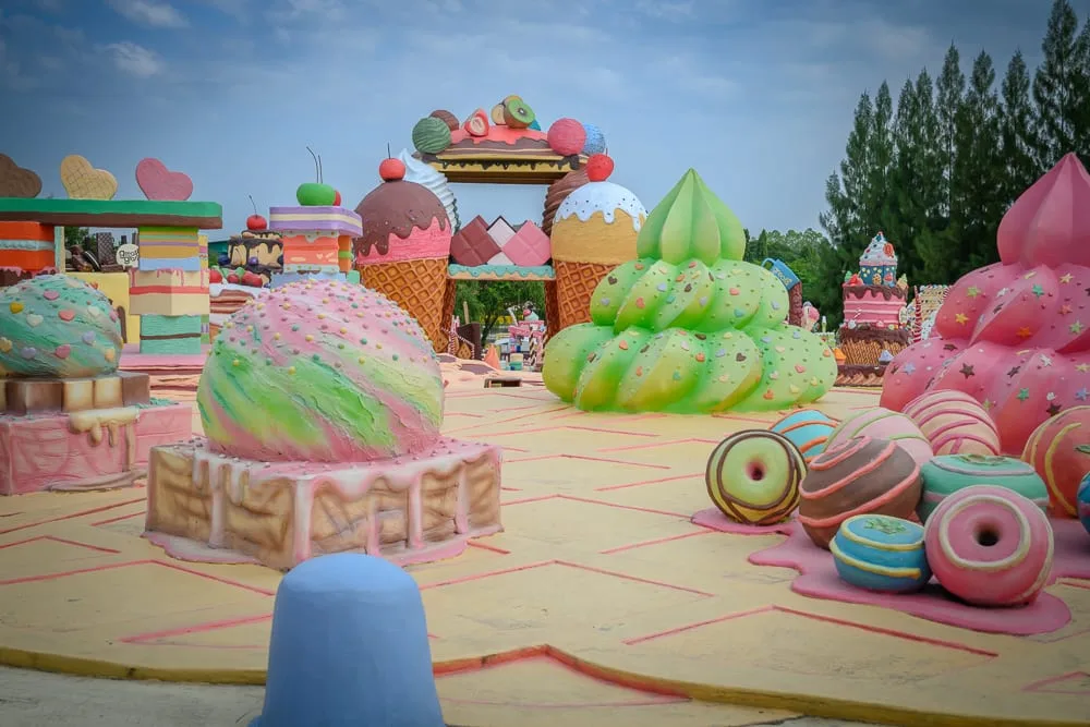 泰國芭達雅GREAT&GRAND Sweet Destination｜戶外樂園，巨型甜點模型，冰淇淋球，甜甜圈，鬆餅，樹木，多雲天空，鮮豔色彩，童話造景，地面格線