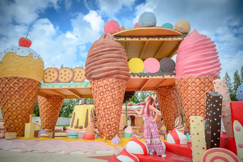 泰國芭達雅GREAT&GRAND Sweet Destination｜巨型冰淇淋模型，建築物，餅乾，草莓，戶外廣場，藍天白雲，粉紅色套裝女子。