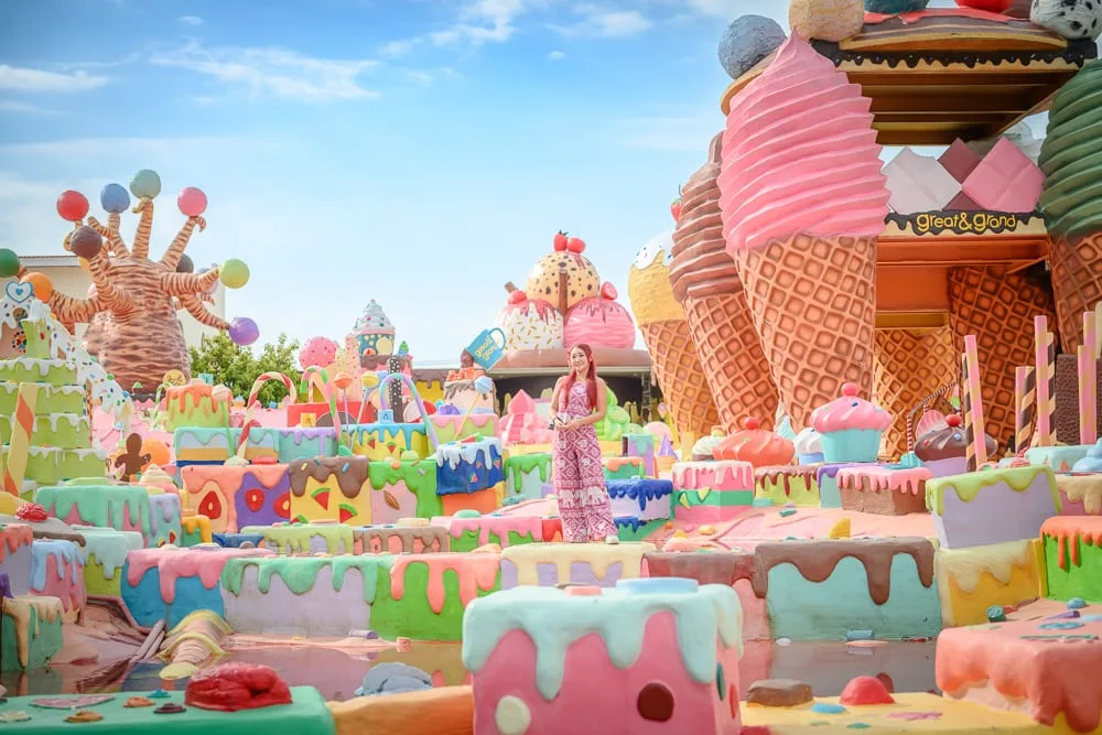泰國芭達雅GREAT&GRAND Sweet Destination｜女子、粉紅連身褲、巨大冰淇淋、甜點造景、蛋糕、糖果樹、藍天、戶外遊樂場。
