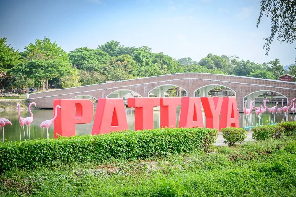泰國芭達雅GREAT&GRAND Sweet Destination｜草坪、綠樹、紅磚拱橋、水池、紅色大字招牌「PATTAYA」、粉紅鶴雕塑。晴朗天幕下，戶外綠意盎然，水