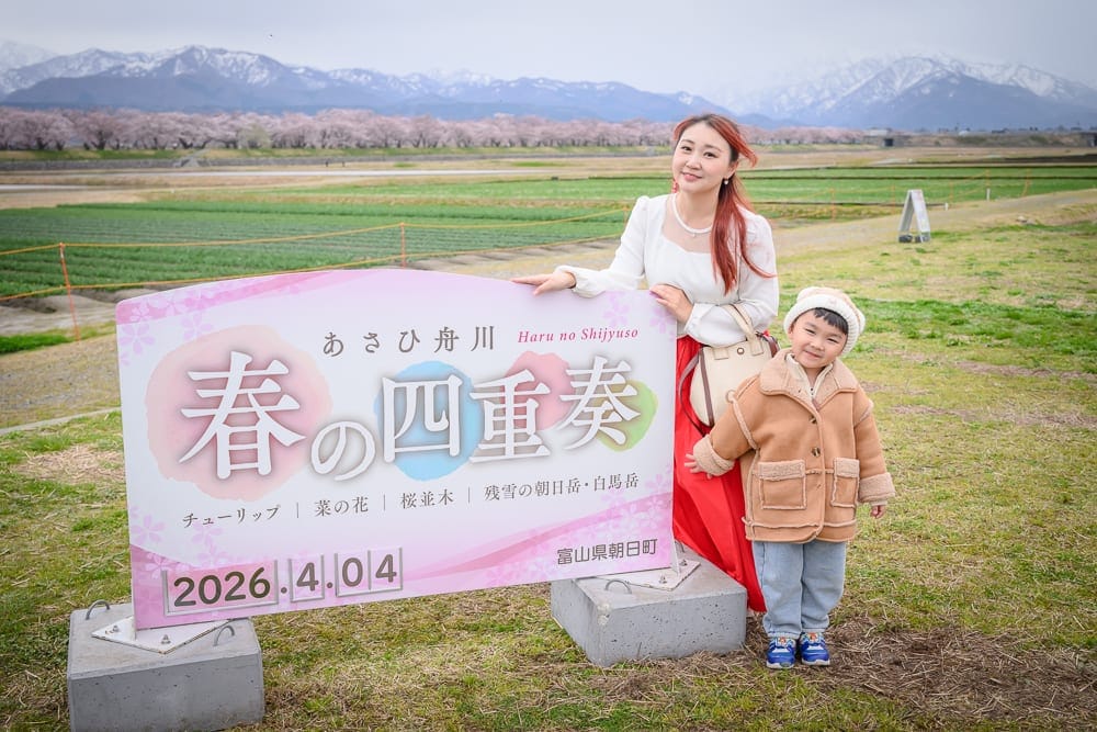 日本富山春之四重奏完整攻略|櫻花、雪山、鬱金香絕景與停車預約指南 12 日本富山-春之四重奏|婦人、兒童、標示牌、草地、遠山,戶外自然場景,明亮春日氛圍。
