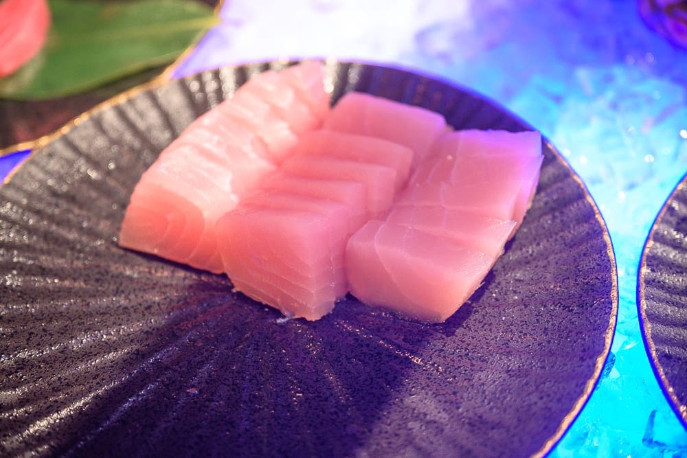 嘉義長榮文苑酒店｜料理、生魚片、黑盘子、冰塊，粉紅色的生魚片切片整齊擺放在黑色扇形盤上，周圍有藍色燈光照耀的碎冰，呈現