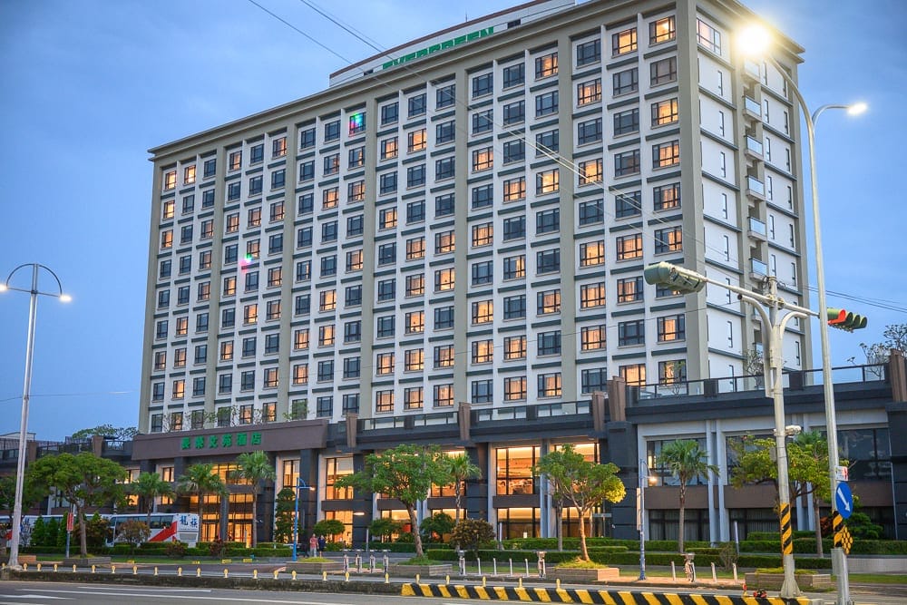 嘉義長榮文苑酒店｜黃昏傍晚時分，大型現代飯店建築，街道，路燈，植栽，飯店，窗戶燈光，藍色天空，寧靜的城市街景。
