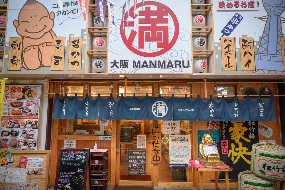日本福岡麵包超人兒童博物館 in 購物商場完整攻略|親子必玩設施與購票全指南 10 日本福岡-福岡麵包超人博物館|招牌、燈籠、布帘、店面、人形立牌,充滿日本大阪風味的居酒屋門面,木質裝潢搭配醒目的紅色圓形標誌與白色