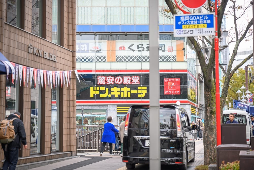 日本福岡麵包超人兒童博物館 in 購物商場完整攻略|親子必玩設施與購票全指南 9 日本福岡-福岡麵包超人博物館|街道、大樓、汽車、行人、招牌,白天都市街景,行人走在人行道上,黑色休旅車停在路邊,背景有多層商業大樓
