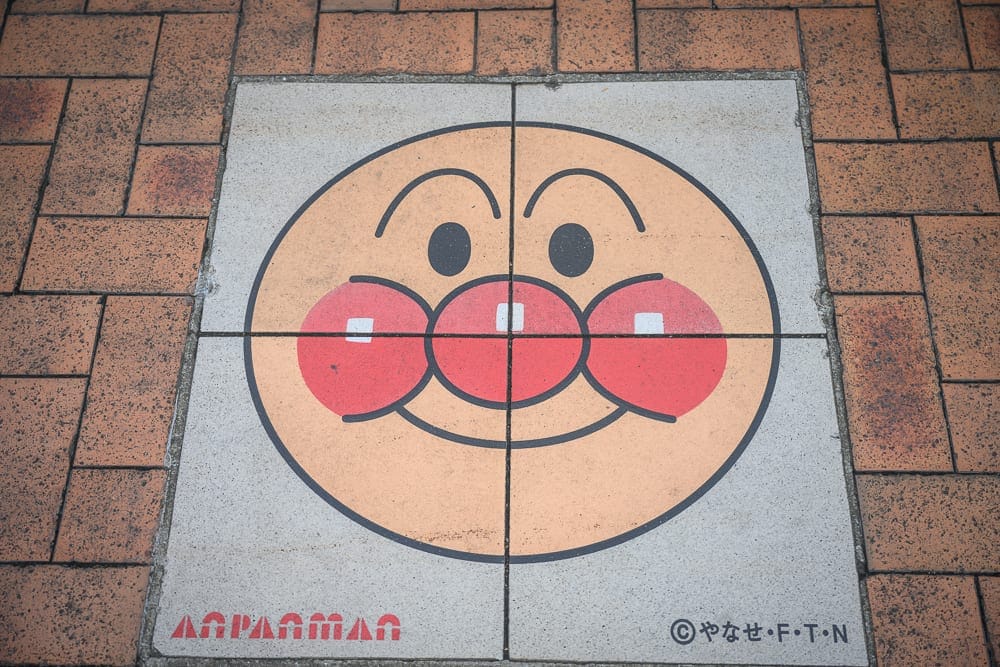 日本福岡麵包超人兒童博物館 in 購物商場完整攻略|親子必玩設施與購票全指南 8 日本福岡-福岡麵包超人博物館|街道,地磚,麵包超人,圖案,戶外,人行道,圓形圖案,卡通角色,童趣氛圍,平面視角。