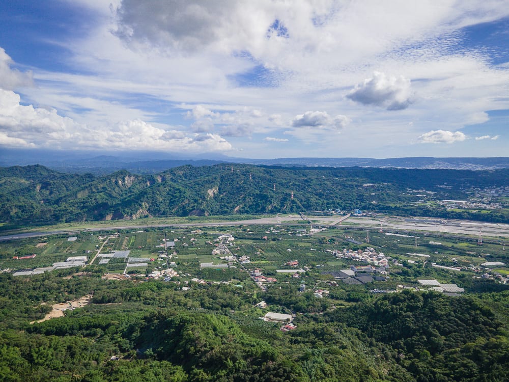 南投九九峰步道｜山脈、河流、村落、農田、道路、藍天、白雲。高空俯瞰山區盆地景觀，寬闊河床蜿蜒穿過綠意盎然的平原，兩側