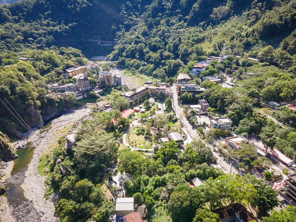 台中統一渡假村 谷關溫泉養生會館完整攻略|親子設施與溫泉泡湯全解析 11 台中谷關統一渡假村|高空俯瞰山谷聚落,溪流、橋梁、建築、茂密綠樹、街道,山坡覆蓋深綠林木,纜線橫跨谷地。