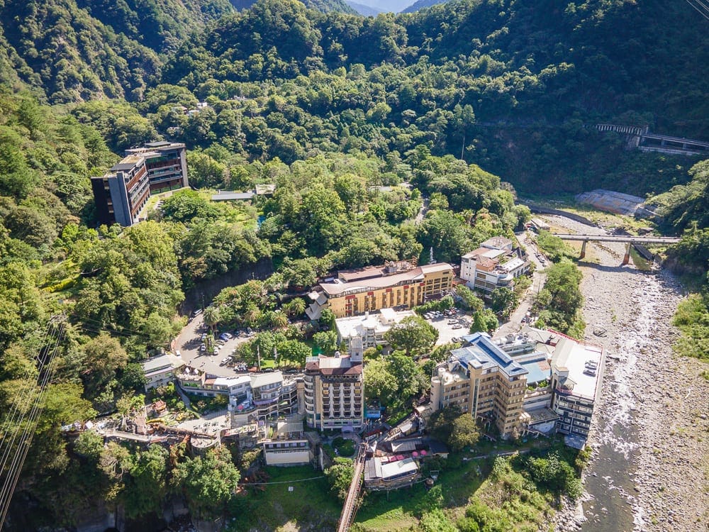 台中統一渡假村 谷關溫泉養生會館完整攻略|親子設施與溫泉泡湯全解析 9 台中谷關統一渡假村|群山,溪流,橋,飯店建築,樹林,山谷,俯瞰視角,道路,車輛,綠意植被,山坡聚落