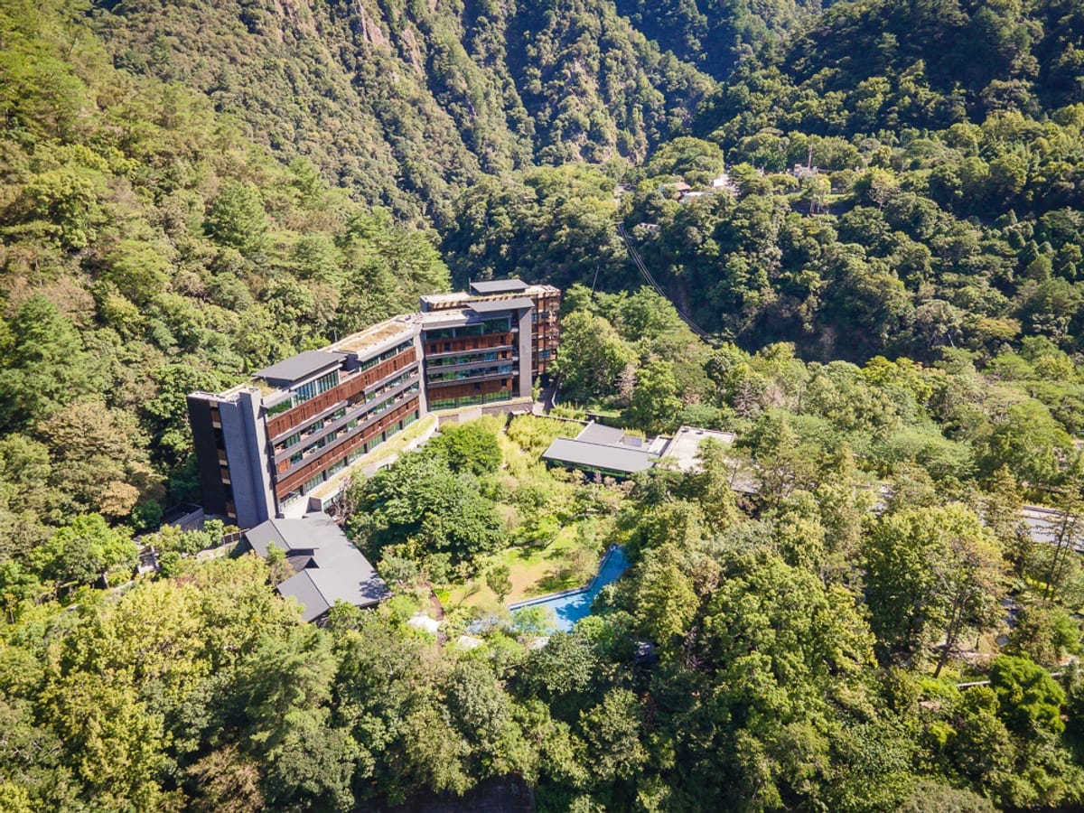 台中統一渡假村 谷關溫泉養生會館完整攻略|親子設施與溫泉泡湯全解析 1 台中谷關統一渡假村|山脈、森林、建築、飯店、游泳池,綠意環繞的山谷中坐落一棟多層樓現代建築,深色外牆搭配大片窗戶,前方空