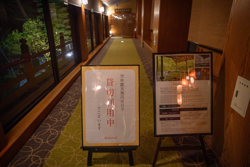 日本福島會津蘆之牧溫泉 大川莊完整攻略|浮舞台三味線演奏與伴手禮精選 10 日本福島-會津大川莊|室內,走廊,告示牌,落地窗,木質牆面。鋪有綠色地毯的長廊內,立著兩塊日文告示牌,左側寫著貸切利用中,