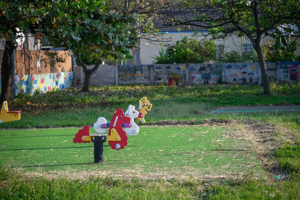 雲林麥寮國小積木公園完整指南|親子遊樂設施與積木造景玩法 13 雲林麥寮國小積木公園|綠地,搖馬遊具,樹木,彩繪矮牆,戶外廣場。人工草皮上設置數座色彩鮮豔的動物造型彈簧搖馬,後方為綠樹與