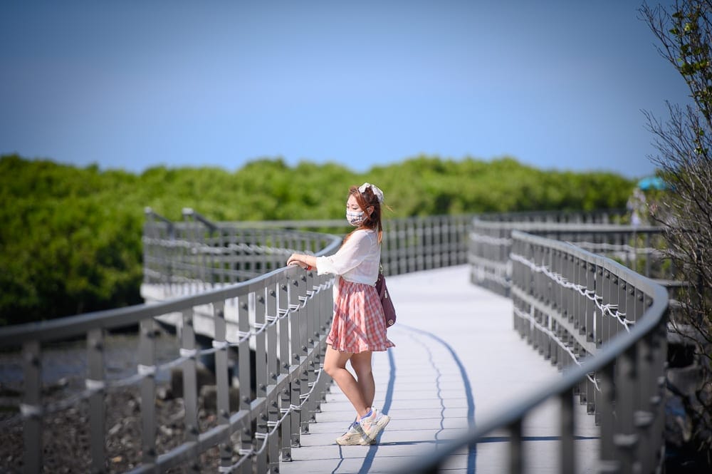 彰化海空步道｜橋、紅樹林、人物、口罩、裙子。女性戴著口罩與頭飾，身穿短袖襯衫與粉色格子短裙，側身站立在戶外白色弧形