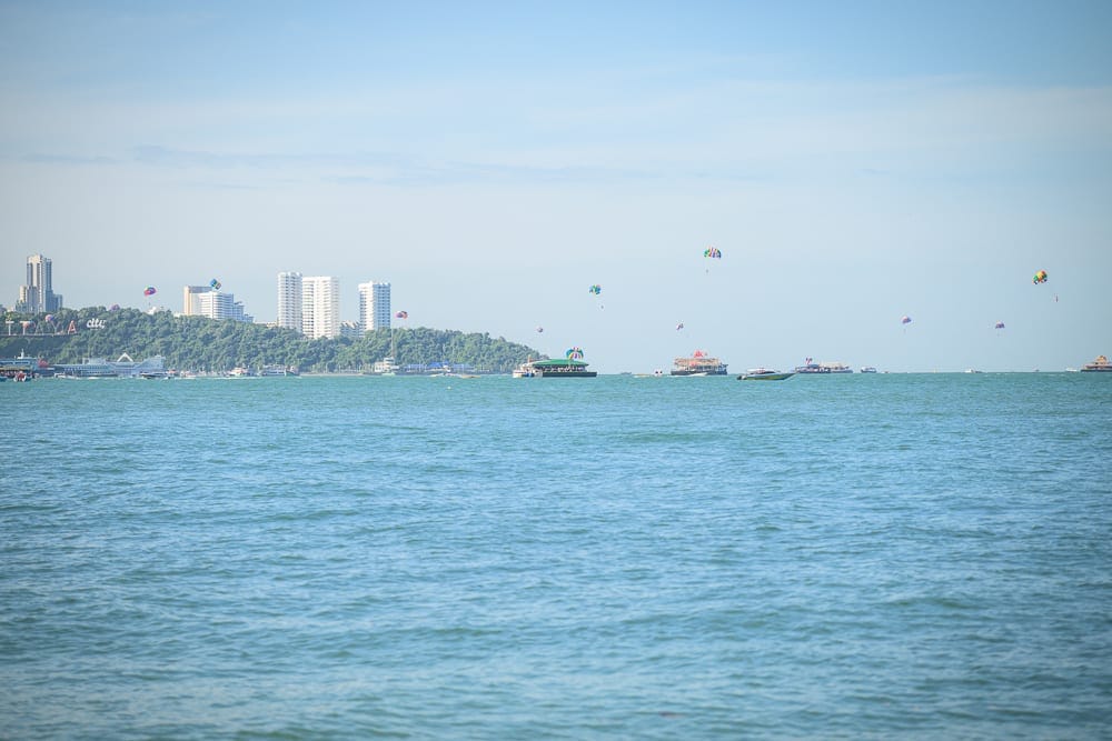 泰國芭達雅LK Emerald Beach完整攻略|泳池海景與接駁服務全解析 11 泰國芭達雅LK翡翠海灘飯店|海邊、高樓、船隻、降落傘、綠樹。晴朗藍天下的大海佔據畫面大半,遠方海岸線坐落著密集白色建築,海面上散