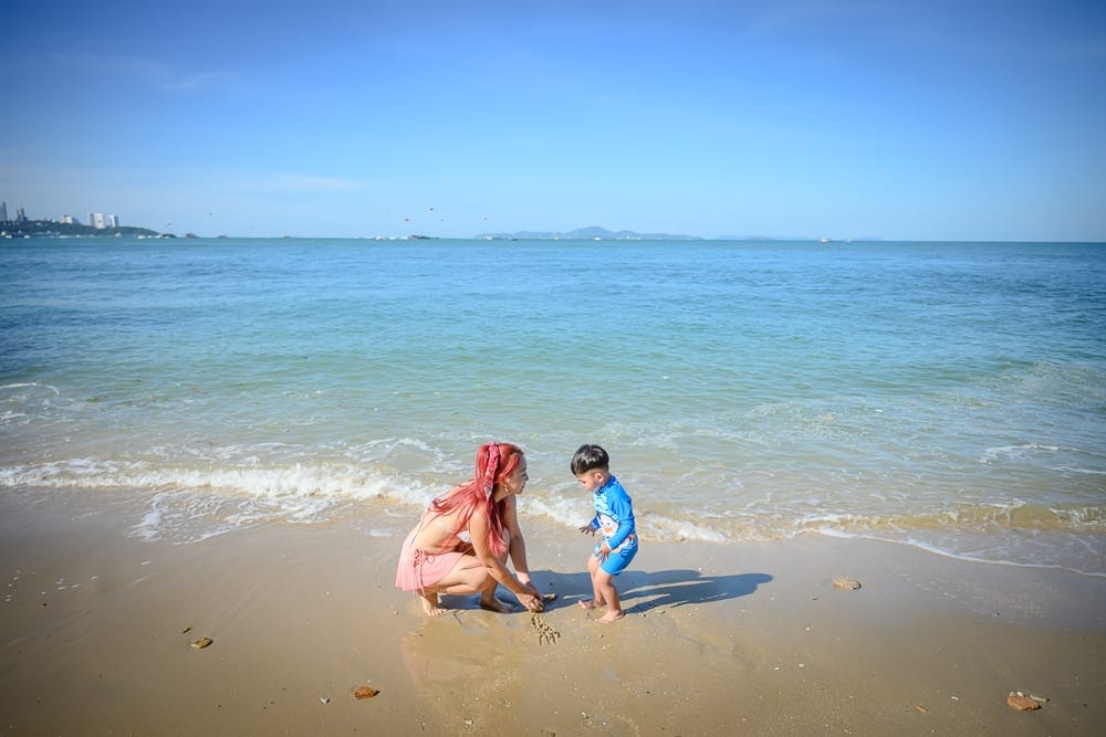 泰國芭達雅LK Emerald Beach完整攻略|泳池海景與接駁服務全解析 8 泰國芭達雅LK翡翠海灘飯店|海邊,沙灘,一對母子,湛藍海水,蔚藍天空。紅髮女子蹲在濕潤沙灘上,小男孩穿著藍色泳衣站在旁邊,兩人面