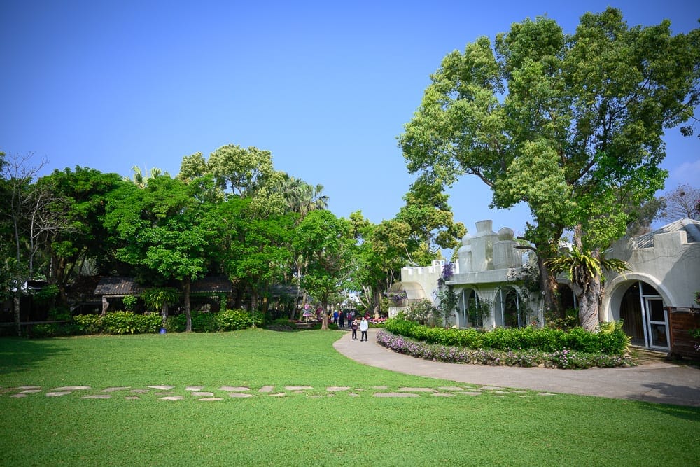苗栗花露農場｜藍天、草坪、綠樹、步道、白色建築，戶外園區，綠意盎然。草地上鋪著石塊，遠處有行人漫步。