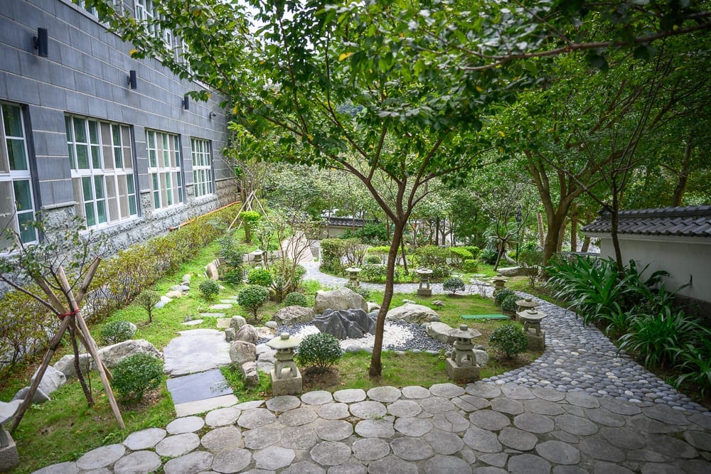 台中統一渡假村 谷關溫泉養生會館完整攻略|親子設施與溫泉泡湯全解析 13 台中谷關統一渡假村|庭園,石燈籠,步道,綠樹,灰磚牆,草地,圓形石板,窗戶