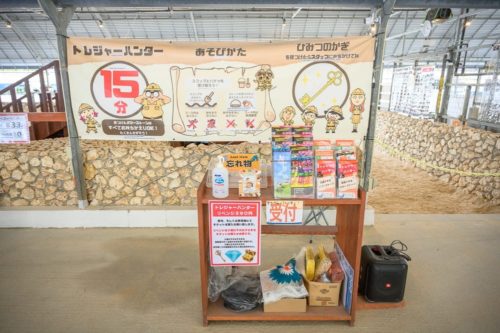 日本沖繩釣魚與探索冒險樂園完整攻略|親子體驗玩法解析 10 日本沖繩釣魚與探索冒險樂園|室內、木櫃、告示布條、宣傳單、石牆,上方懸掛印有日文字母與圖解的黃色長型布條,下方木櫃擺放消毒液、票