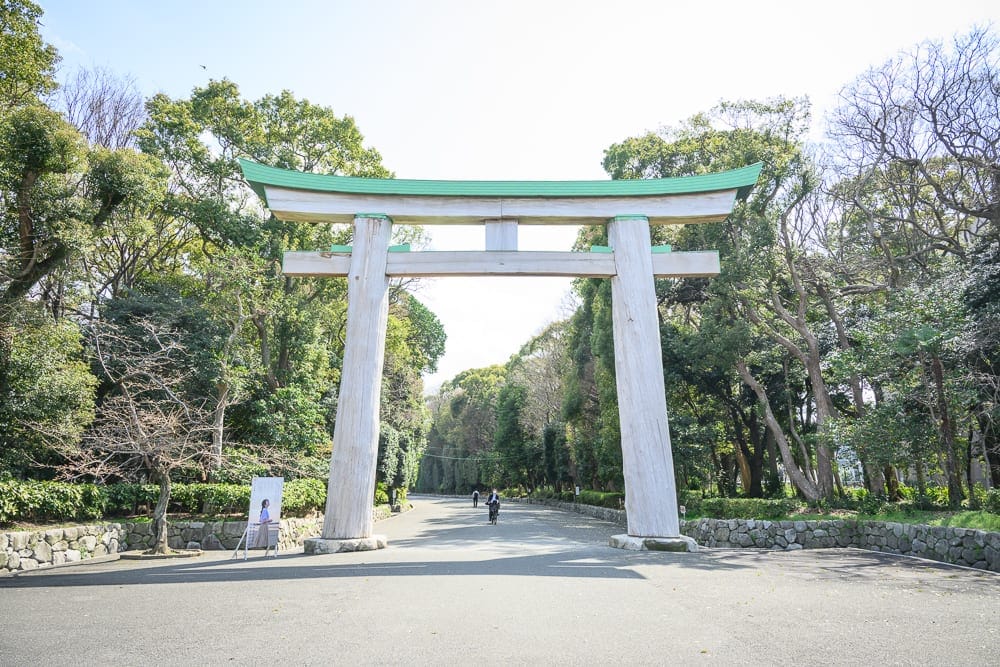 日本福岡-護國神社｜大型木造鳥居，綠色屋頂，石砌矮牆，林道，樹木，單車騎士，戶外。