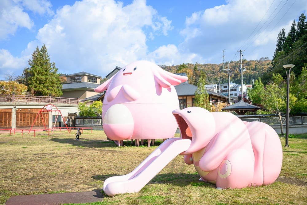 日本福島-吉利蛋公園｜戶外公園，草地，粉紅色寶可夢雕像，吉利蛋造型建築，大舌舔溜滑梯，遠方房屋，藍天白雲，樹木