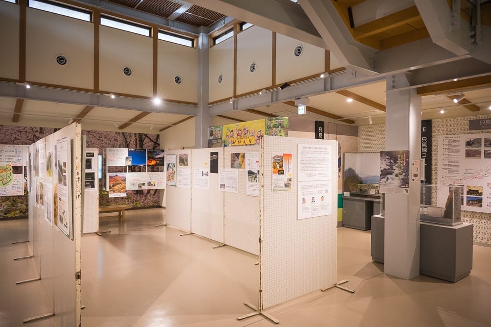 日本福島-吉利蛋公園｜室內、展覽館、展示板、壁板、柱子，空間挑高明亮，牆面排列多張文件與圖片，地板光滑反射天花板燈光，四周