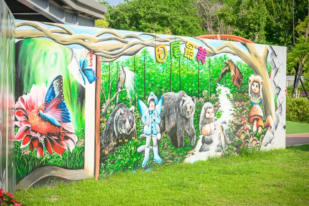彰化田尾怡心園公園｜戶外彩繪牆，森林，熊，精靈，蝴蝶，花朵，草地。彩繪牆面描繪森林奇幻生態，綠草地上立著大型壁畫，畫面包