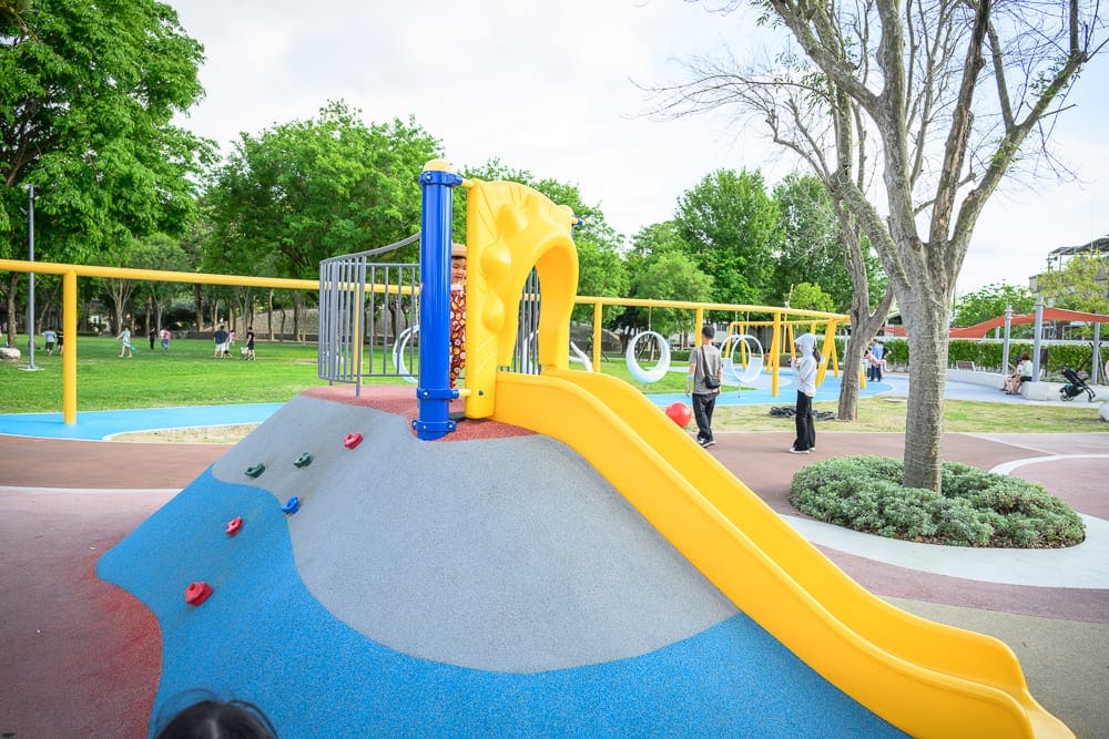 彰化田尾怡心園公園｜戶外公園、遊樂場、溜滑梯、攀岩牆、樹木、草皮、行人、黃色滑梯、藍色地墊。