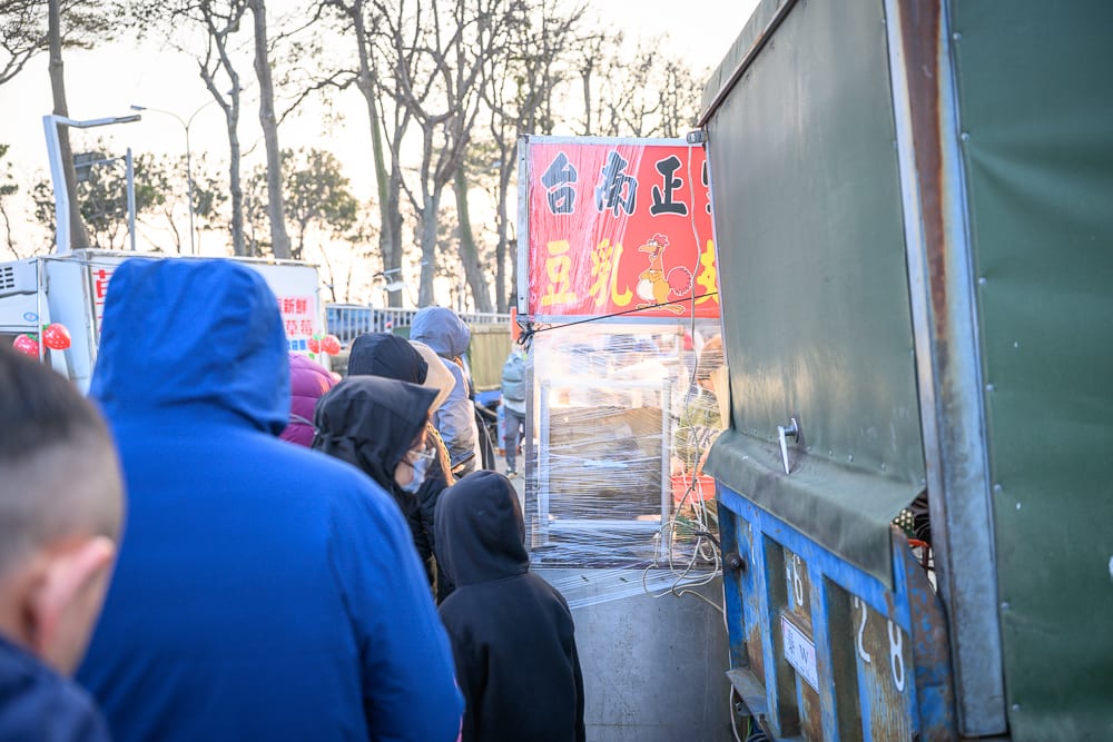 苗栗後龍夜市完整攻略|週日封街市集與在地小吃指南 8 苗栗後龍夜市|戶外市集,排隊人潮,藍色外套,紅色招牌,小吃攤位,貨車,背影。