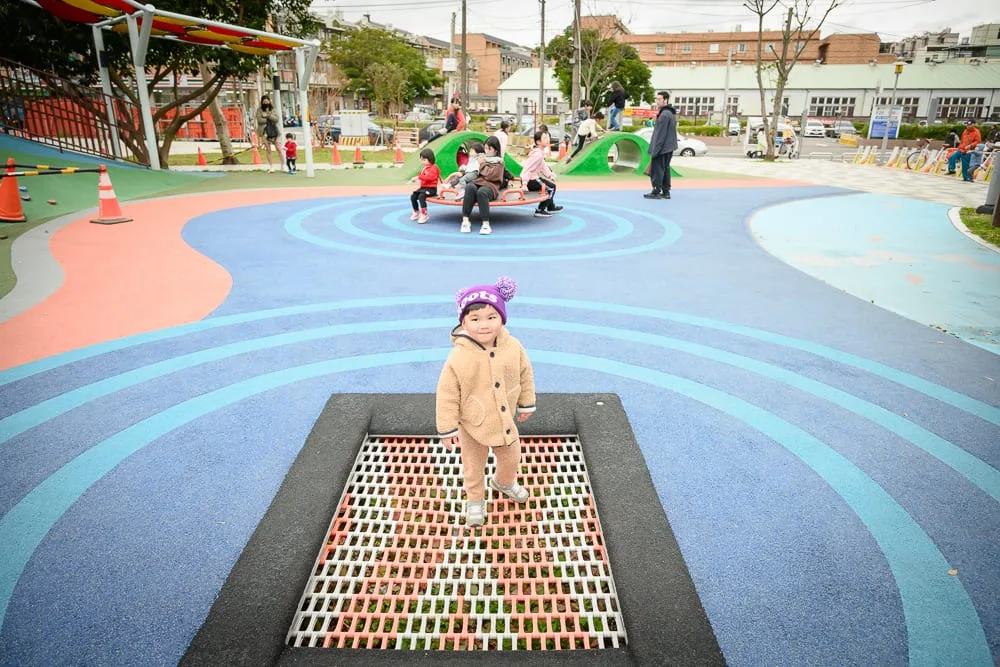桃園民俗文化公園｜戶外公園，彈跳床，小孩，彩色地墊，旋轉遊具，遠處建築，陰天光線