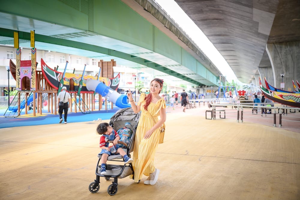 宜蘭礁溪二龍之心公園｜高架橋下，遊樂場，婦人，嬰兒車，小孩，船型遊具，欄杆，行人。