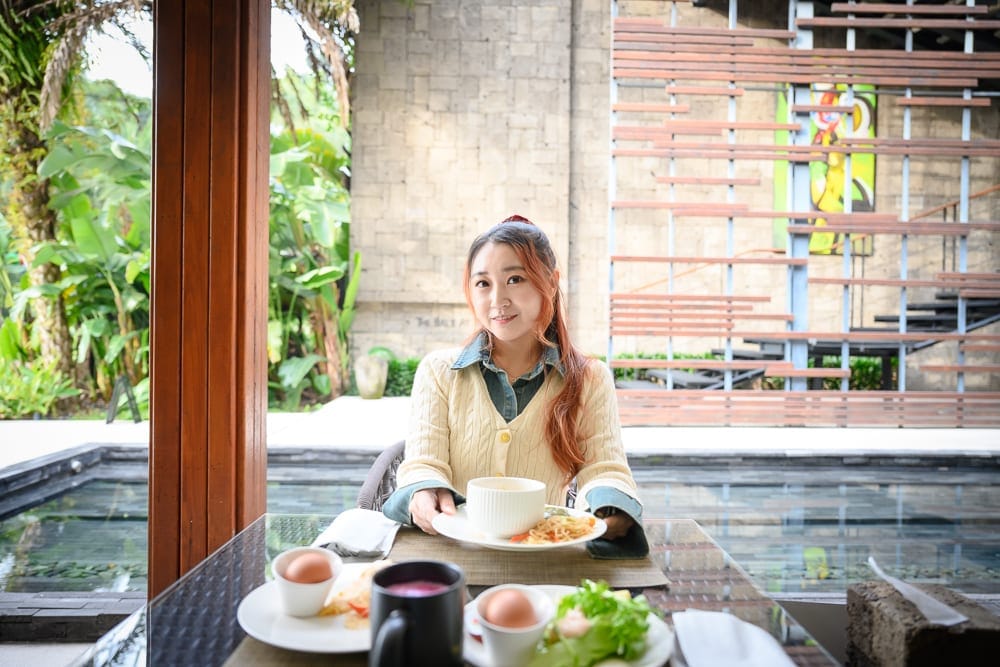 南投牛眠埔里｜室內、料理、女性、木柱、水池、石牆。長髮女性坐在戶外露台座位，桌上擺放白色餐盤盛裝蛋、沙拉與主食。背