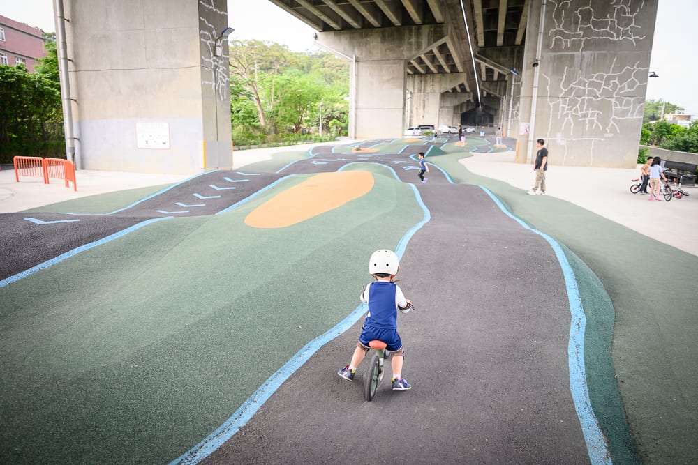 新竹風火輪公園｜橋墩、高架橋下、車道、兒童、平衡車、滑步車、公園，戴安全帽的孩童騎著無踏板單車，行駛在灰色波浪狀的車