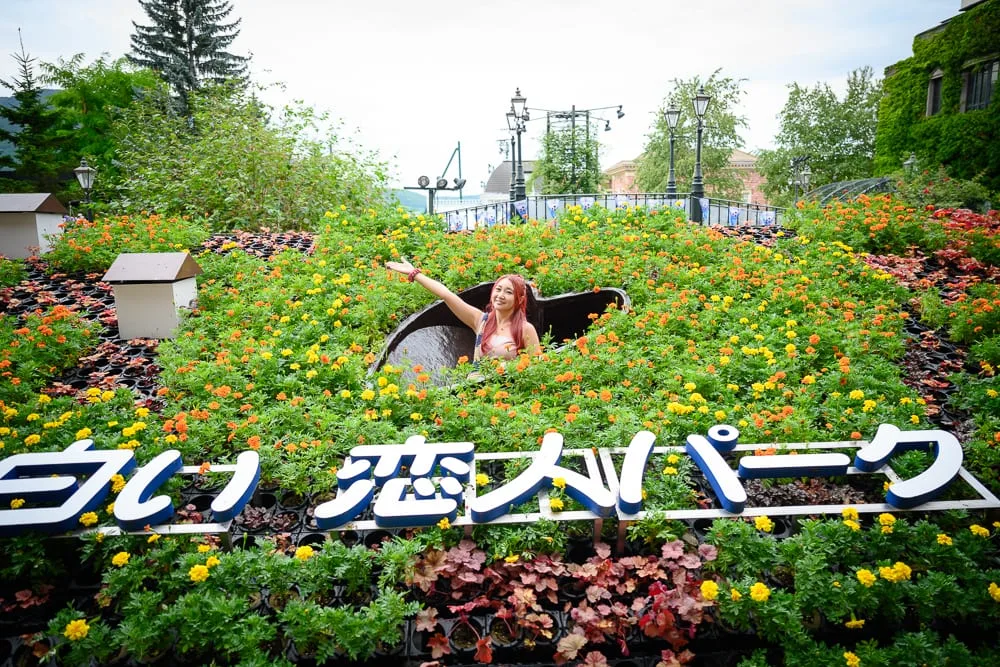日本札幌-白色戀人觀光工廠｜女性，花園，日文字招牌，花壇，綠樹，戶外，建築物，噴泉，路燈，陰天。
